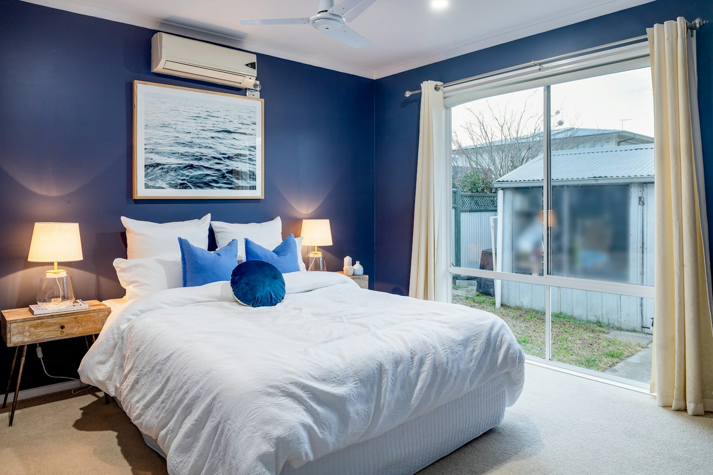 Schlafzimmer mit marineblauen Wänden und beleuchteten Lampen auf Nachttischen.